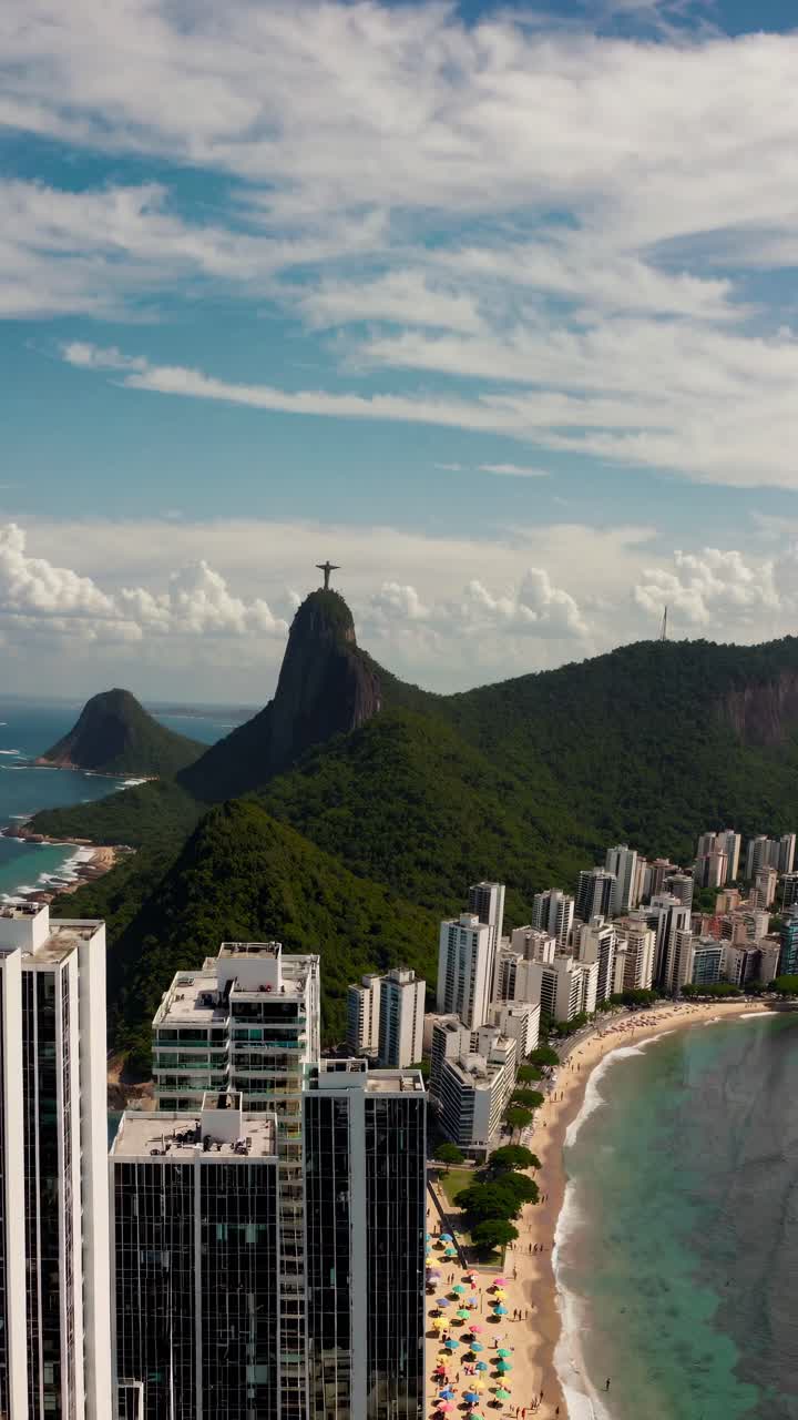 Aerial video view of a coastal city with lush green mountains, high-rise buildings, and a sandy