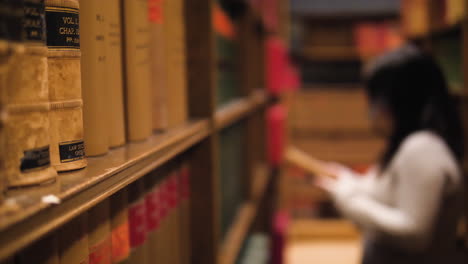 reveal shot coming from behind a bookshelf, as a woman getting off a book in the blurred background, focus on books in the foreground