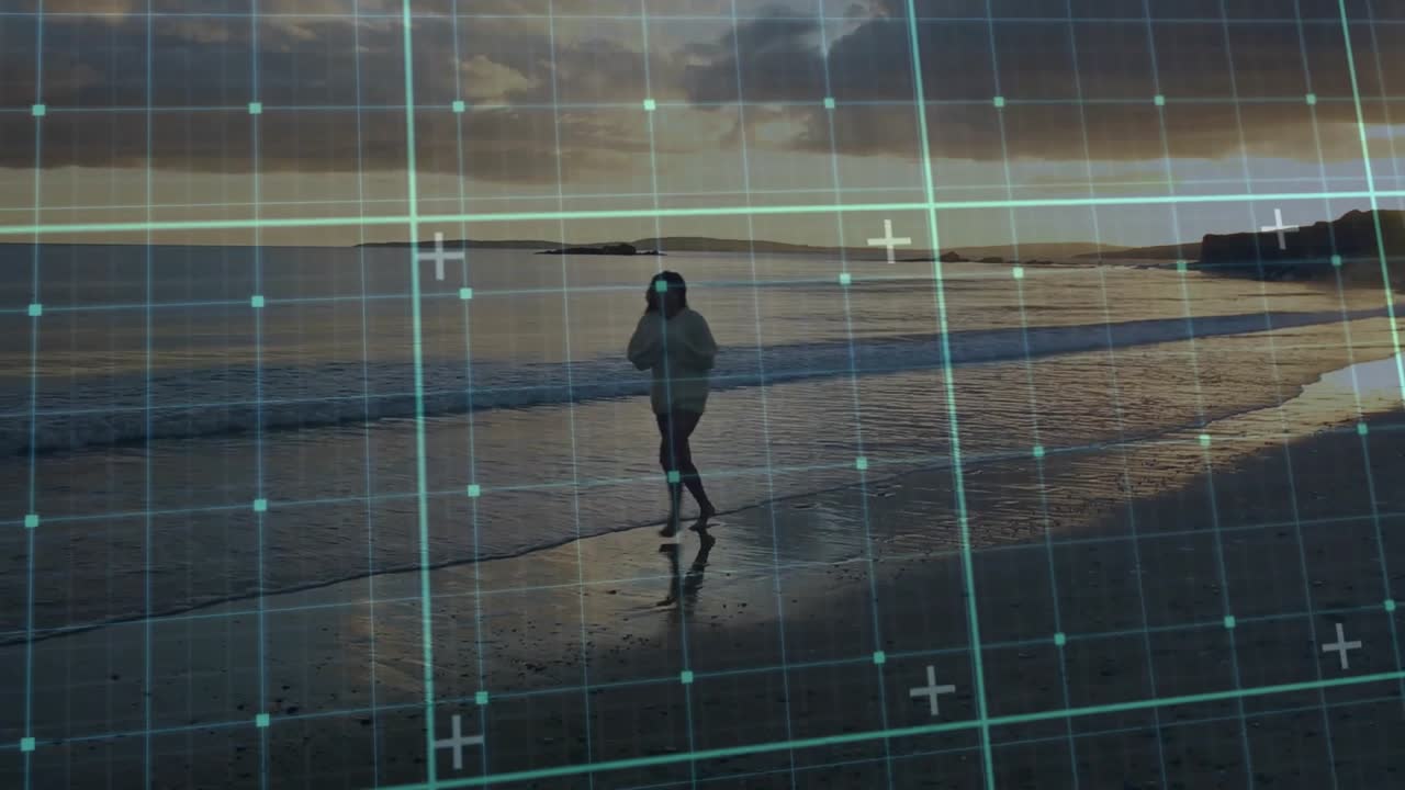 Overlay a griglia che appare gradualmente, rivelando una spiaggia al tramonto, mentre una donna a piedi nudi cammina sulla sabbia per una demo tecnologica.