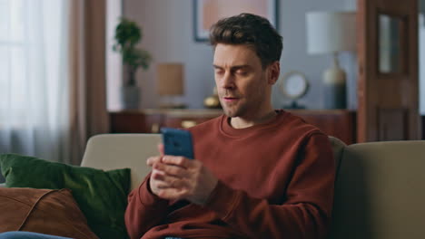 angry man swiping cellphone screen reading message with bad news at home closeup