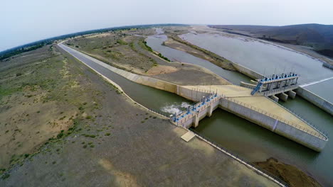 Aerial-view-of-spillway-of-a-dam,-Beautiful-majestic-mountains-in-the-back-of-the-dam