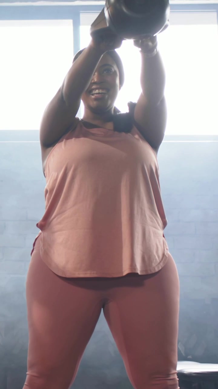 Video verticale: Donna che tiene un kettlebell in abbigliamento rosa che esegue swing con cerniera all'anca in palestra per il fitness