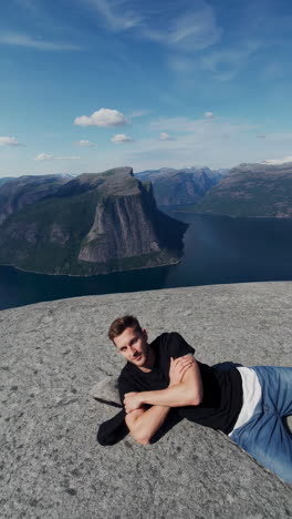 man relaxing on a cliff edge overlooking a scenic fjord landscape