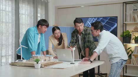 아시아 엔지니어 그룹은 태양 전지 패널 하우스 모델과 함께 사무실에서 노트북 작업에 대해 논의합니다.