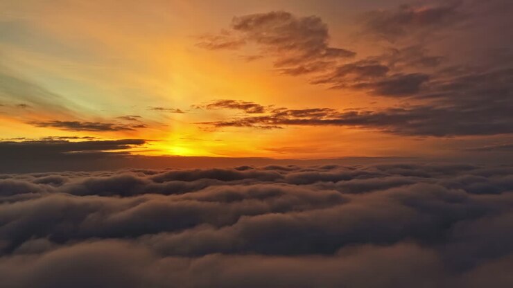 Distesa di nuvole rilassante dai toni caldi che si estende sotto l'orizzonte all'alba, mentre colori luminosi si allungano nel cielo