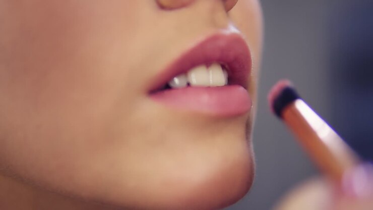 Close Up view of a professional makeup artist applying lipstick on model's lips working in beauty fashion industry. Close Up view