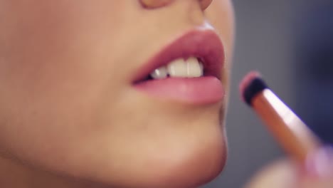 Close Up view of a professional makeup artist applying lipstick on model&#039;s lips working in beauty fashion industry. Close Up view