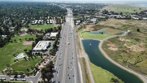 Aerial-view-of-suburbs-dense-trees-rooftop-houses-pine-trees-cars-freeway-101-marsh-golf-course-pan-sideways