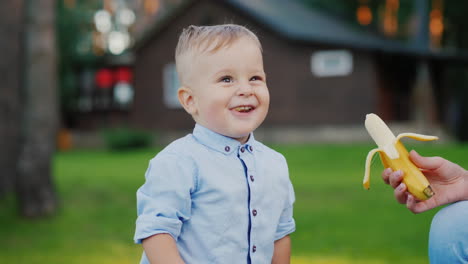 joyful baby eats a banana that his mother gives him