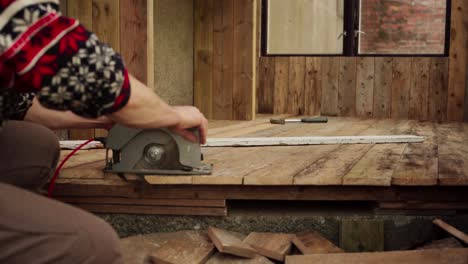 vista recortada de un hombre cortando un piso de tabla de madera usando una sierra circular eléctrica