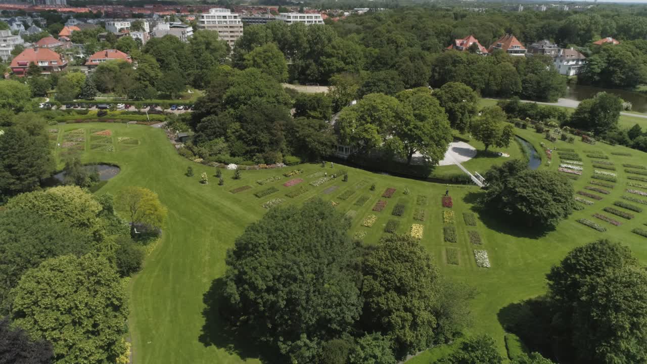 Dronebeelden in slow motion van een Nederlandse bloementuin in Den Haag met passerende toeristen en meeuwen, tijdens zonnig weer.