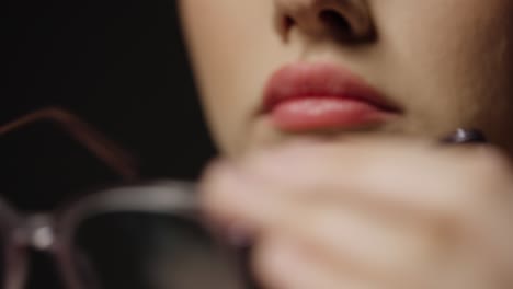 primer plano de una mujer joven con labios hermosos respirando en las lentes de sus gafas para limpiarlas después para una mejor vista y una mejor vista frente a un fondo negro en cámara lenta
