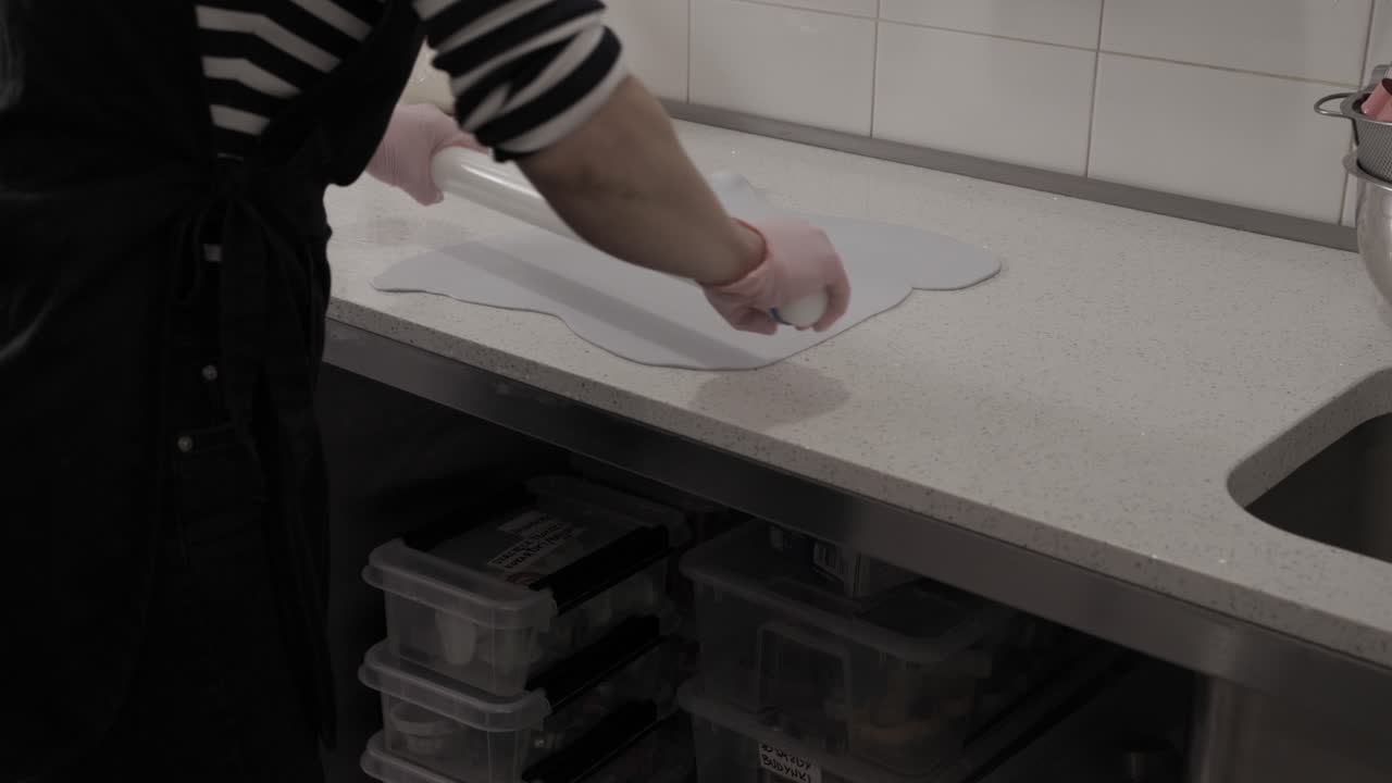 Uma pessoa esticando uma folha fresca de glacê para decorar biscoitos amanteigados artesanais em uma confeitaria, 4K.