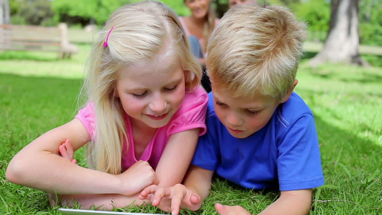 hermano y hermana usando una tableta pc juntos mientras yacen en la hierba antes de sonreír a la cámara