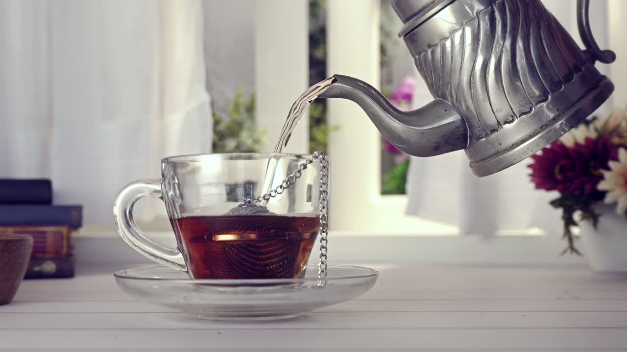 Verter té caliente en una taza de cristal desde una tetera vintage