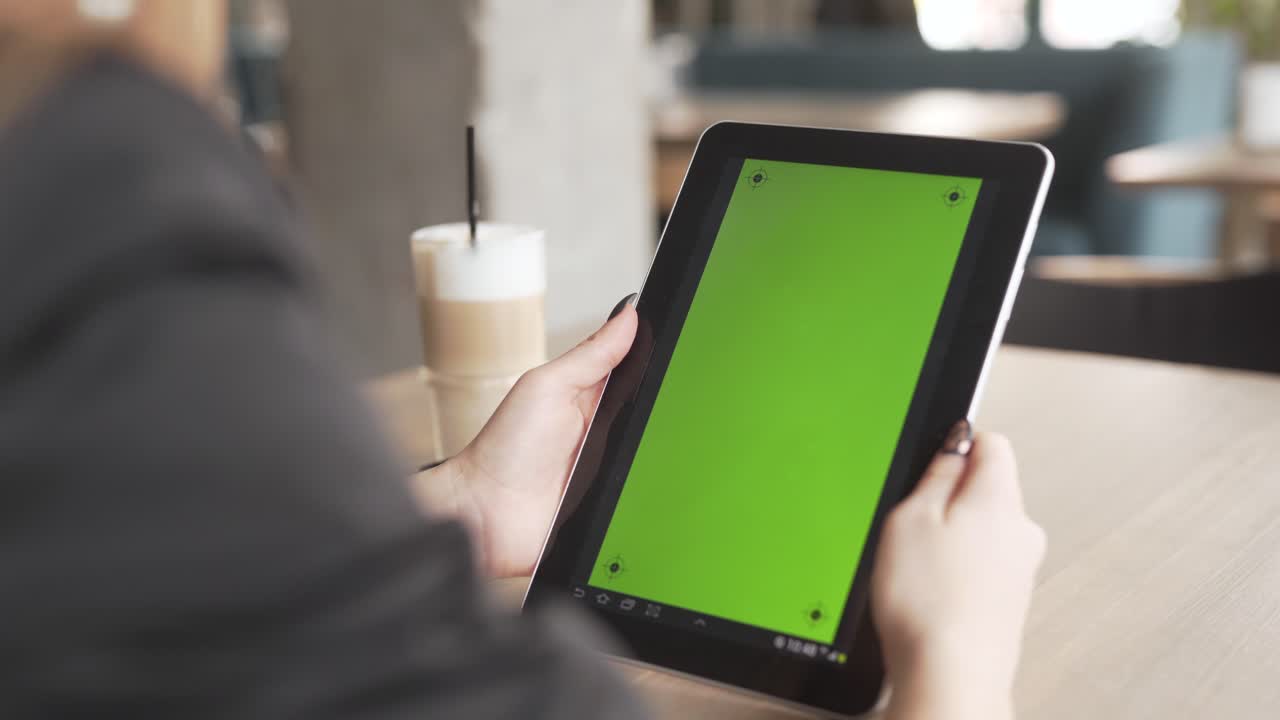 las manos de una mujer de negocios sostienen una tableta en un café con la pantalla frente a la cámara