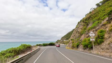 a car travels along the picturesque great ocean road, flanked by lush greenery and ocean views under a cloudy sky