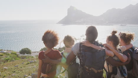 group of young friends hiking standing on cliffs by coast and looking at beautiful view