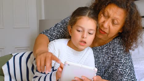 chica usando tableta digital con la abuela en el dormitorio 4k