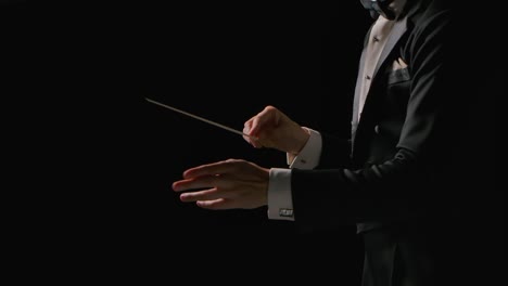 symphony orchestra conductor wearing suit is directing musicians with movement of baton, isolated on black background. conducting, directing a musical performance with visible gestures. close up