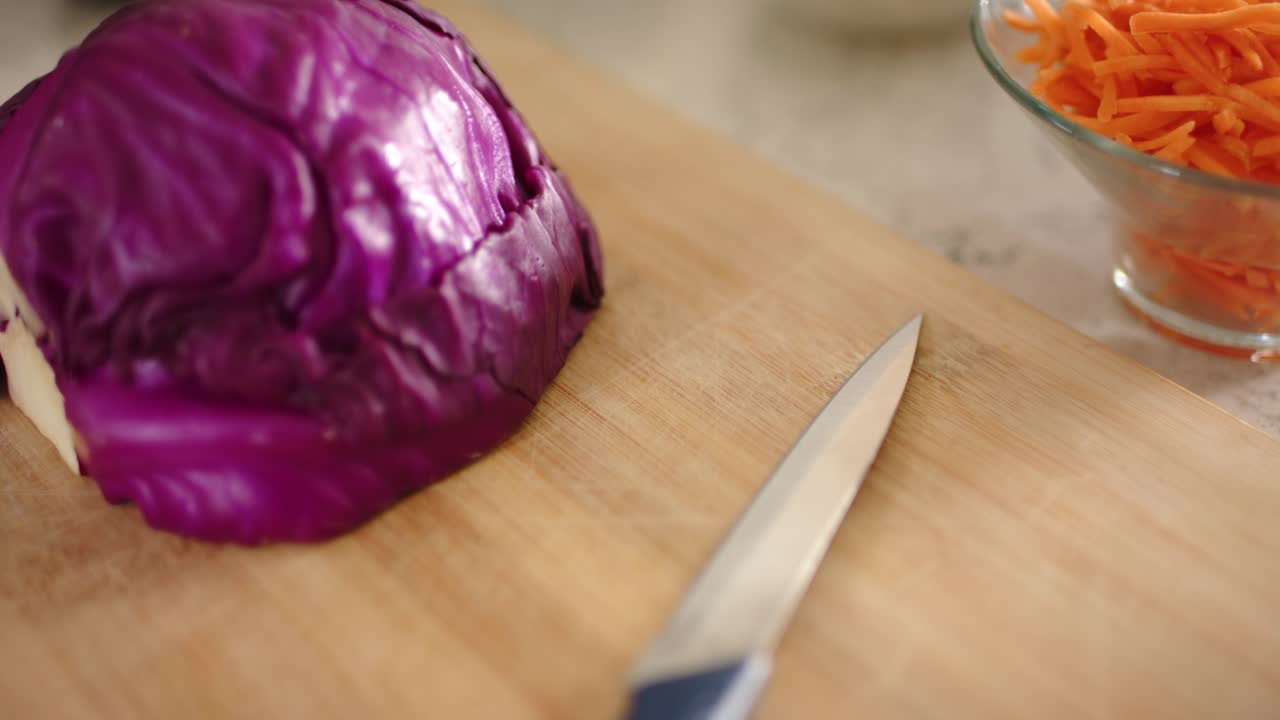 Daylight shifting camera holding cutting board on counter with cabbage, knife and carrots for prep