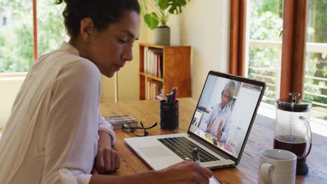 Mujer-Afroamericana-Tomando-Notas-Mientras-Realiza-Una-Videollamada-En-Una-Computadora-Portátil-En-Casa