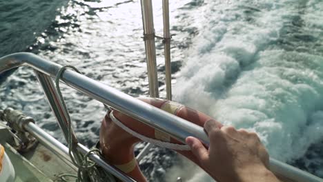 hand holding a rail in the back of a boat-ferry while sailing in ocean