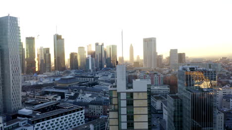 AERIAL:-Confident-Young-Man-on-Skyscraper-rooftop-in-Skyline-of-Frankfurt-am-Main,-Germany-with-Beautiful-Sunlight-in-Winter-Haze