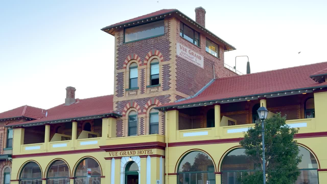 A detailed view of a historic building's facade with arched windows and a tree in the foreground.