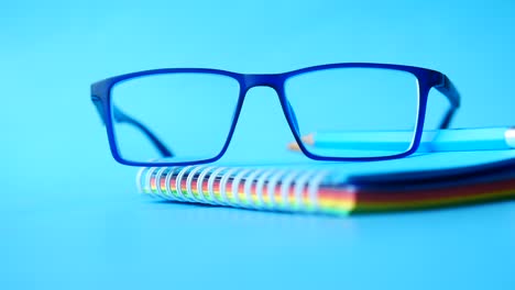 glasses, pencil, and notebook on blue background