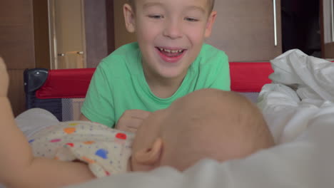 A-boy-in-a-green-T-shirt-happily-looking-at-his-baby-sister