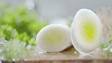chef cutting a leek stem with a sharp knife on a wooden water covered cutting board, macro and slow motion