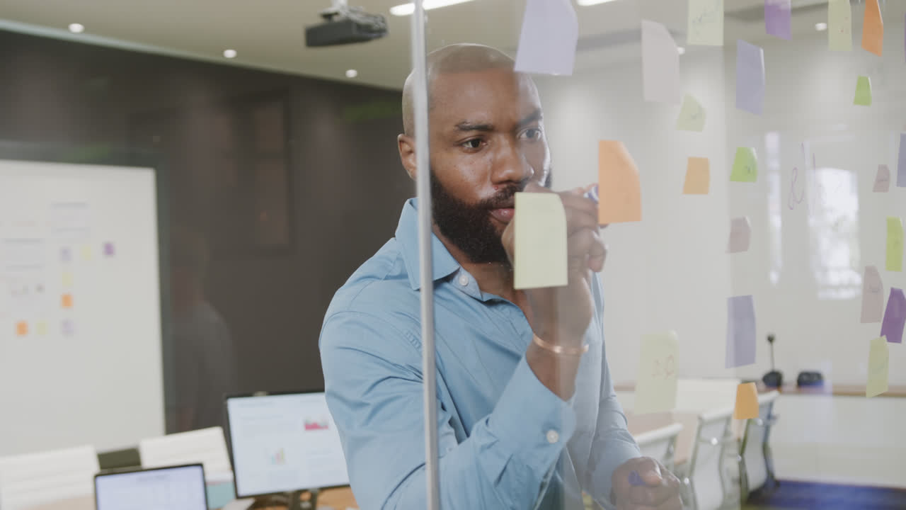 African american businessman brainstorming, making notes on glass wall in office in slow motion