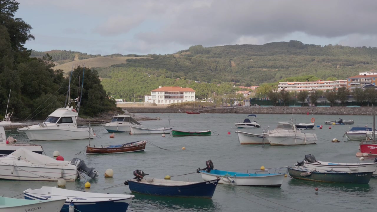 Boats mooring on the tranquil waters of Plentzia harbor, with green hills and coastal buildings creating a serene travel scene