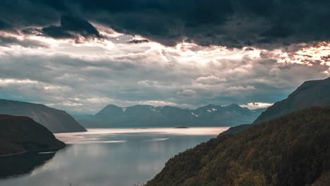 rays of the setting sun pierce through the dense stormy clouds whirling above the calm fjord