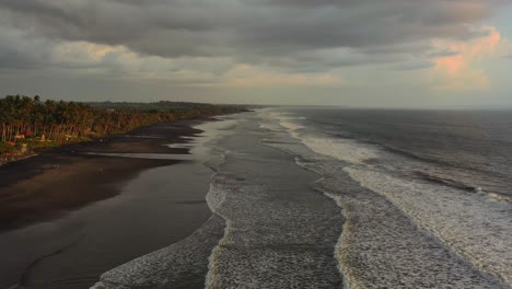 El-Carro-Aéreo-Se-Aleja-De-La-Playa-Vacía-De-Arena-Negra-En-Bali,-Indonesia,-Durante-La-Puesta-De-Sol