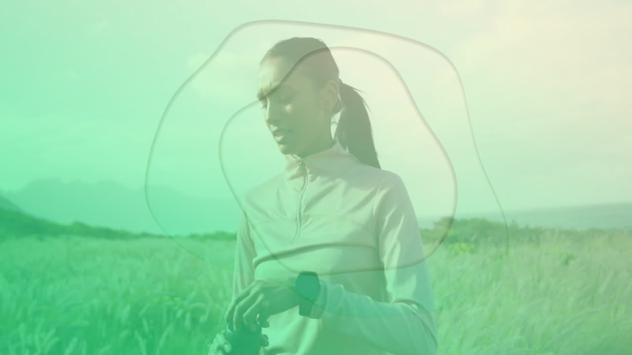 female athlete checking smartwatch in coastal grassland, showing animated fitness graphs