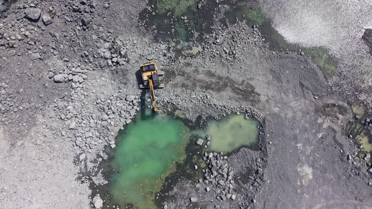 Granite quarry in operation with heavy machinery digging and exploring water-filled pits on a bright day