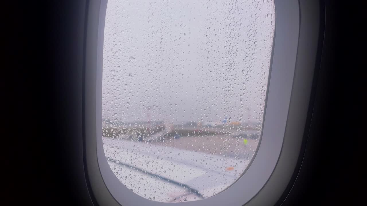 Rainy airplane window view with droplets and airport visible