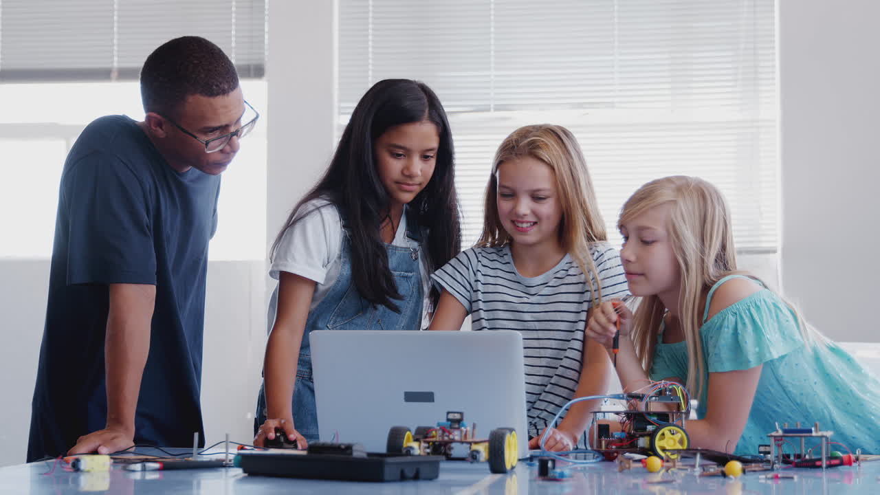 maestra con estudiantes mujeres construyendo y programando un vehículo robot en la clase de codificación de computadoras de la escuela