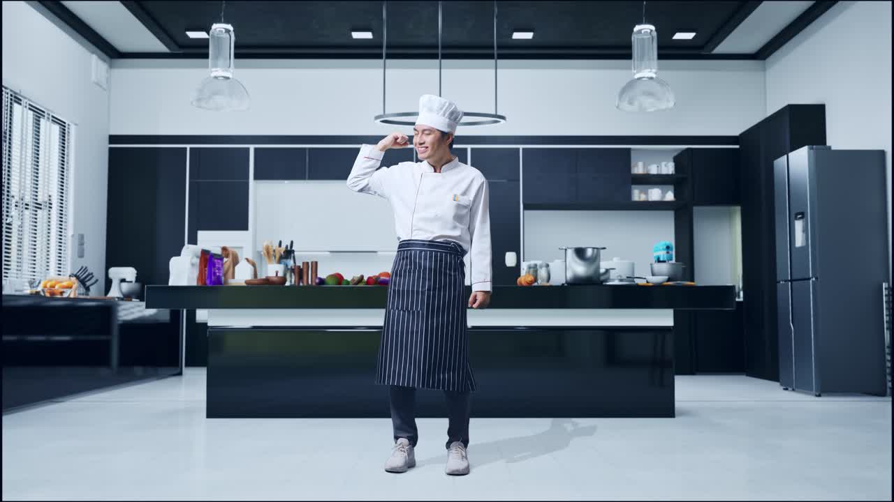 cuerpo lleno de hombre asiático chef sonriendo y flexionando su bíceps mientras está de pie en la cocina de casa