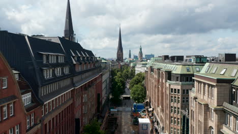 Forwards-fly-above-street-in-historic-city-centre.-Several-towers-of-historic-landmarks-in-distance.-Free-and-Hanseatic-City-of-Hamburg,-Germany