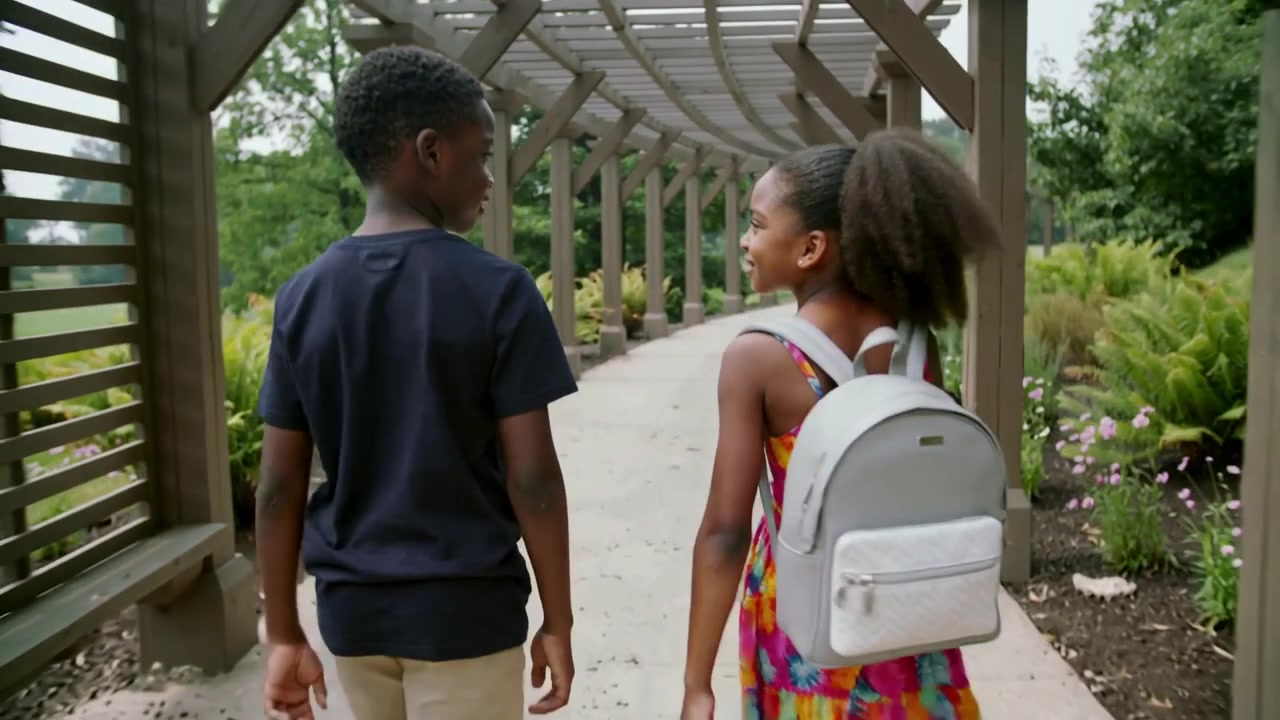 Entering pergola siblings walking chatting paved path girl in dress with backpack heading to school
