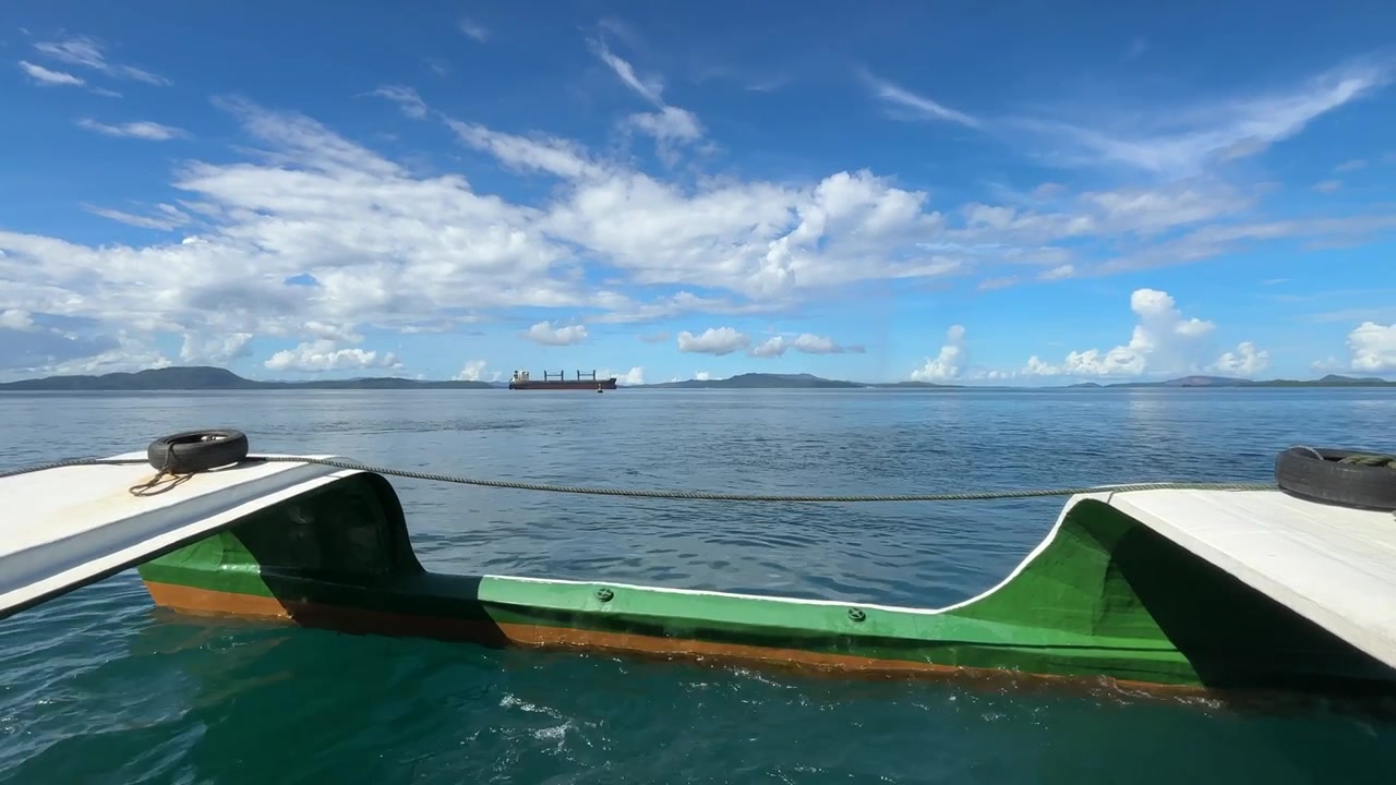 Vista da una barca dell'oceano e di una nave distante nelle Filippine sotto un cielo blu.