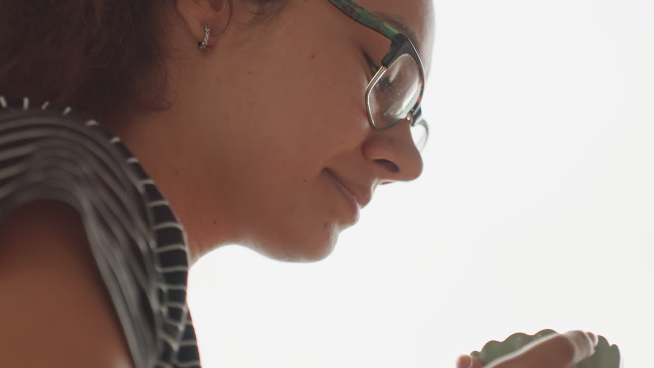 Ospite donna che annusa una tazza di tè. Momento intimo di degustazione con occhi chiusi, espressione concentrata, sorso delicato e inspirazione, atmosfera da boutique hotel, camicia a righe e occhiali, inquadrature da ritratto cinematografico.