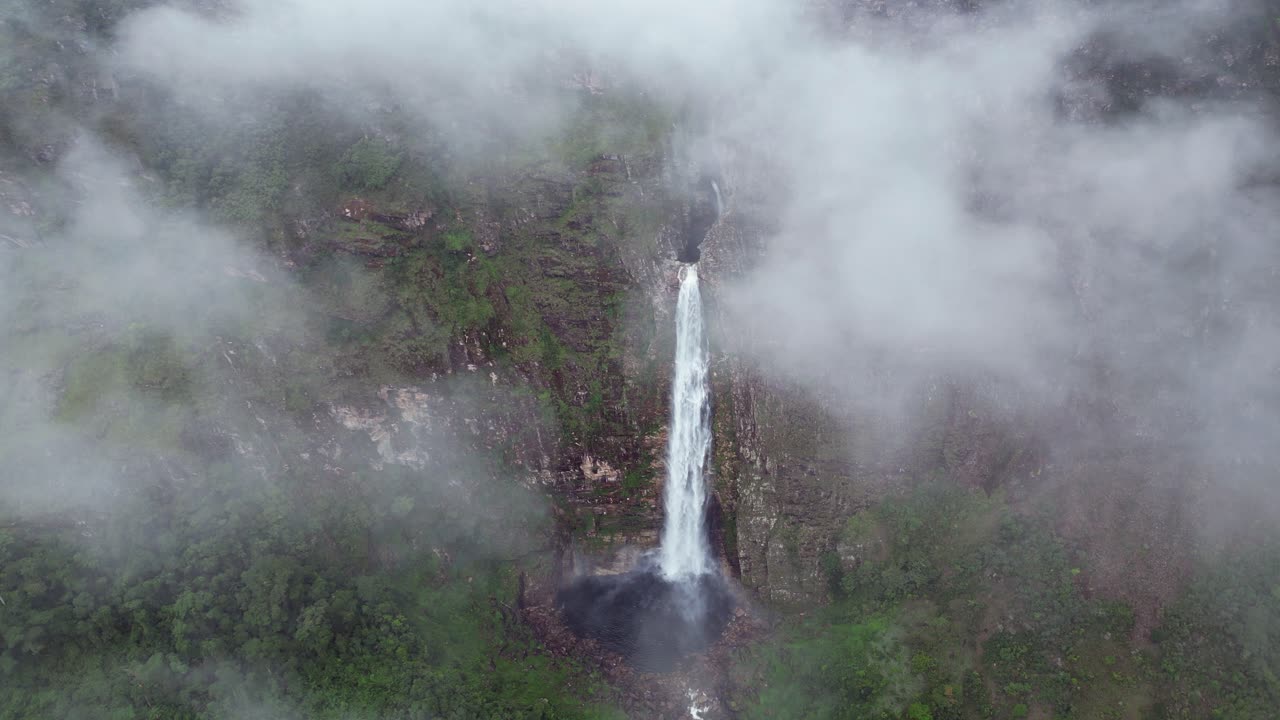 Fluffy clouds float past Casca D'anta waterfall on cliff in rural Brazil