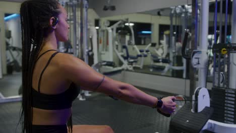 fotografía de perfil de una chica en forma usando una máquina de fila en un gimnasio vacío temprano en la mañana