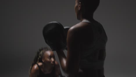 studio shot of woman wearing boxing gloves sparring with trainer 2