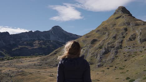 blonde woman admiring beautiful mountain landscape and covers her eyes from the sun