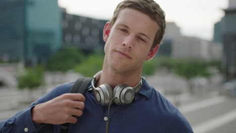 Primer-Plano-Retrato-De-Un-Atractivo-Hombre-Caucásico-Estudiante-Se-Pone-Auriculares-Escuchando-Música-Relajado-Mirando-Confiado-A-La-Cámara-En-El-Fondo-De-La-Ciudad